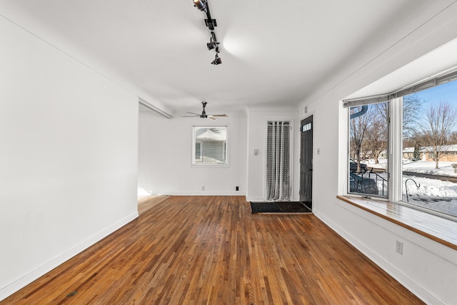 interior space featuring rail lighting, a ceiling fan, baseboards, and wood-type flooring