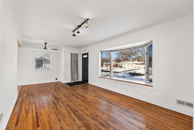 unfurnished living room with visible vents, track lighting, ceiling fan, baseboards, and hardwood / wood-style flooring