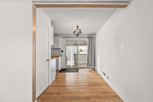 interior space featuring visible vents, baseboards, light wood-style floors, and an inviting chandelier