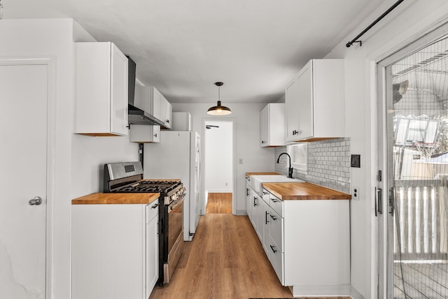 kitchen with stainless steel range with gas stovetop, a sink, wood counters, white cabinetry, and light wood-type flooring