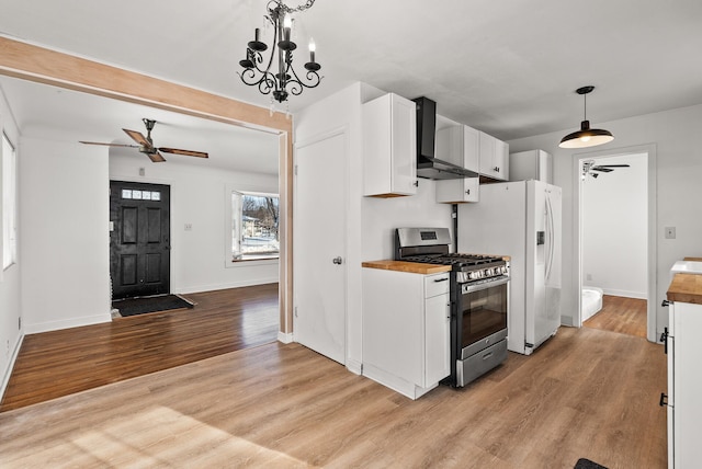 kitchen featuring wall chimney range hood, light wood finished floors, white cabinets, and stainless steel range with gas cooktop