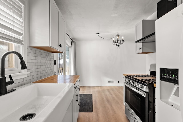 kitchen with a sink, backsplash, light wood-style floors, white fridge with ice dispenser, and stainless steel range with gas stovetop