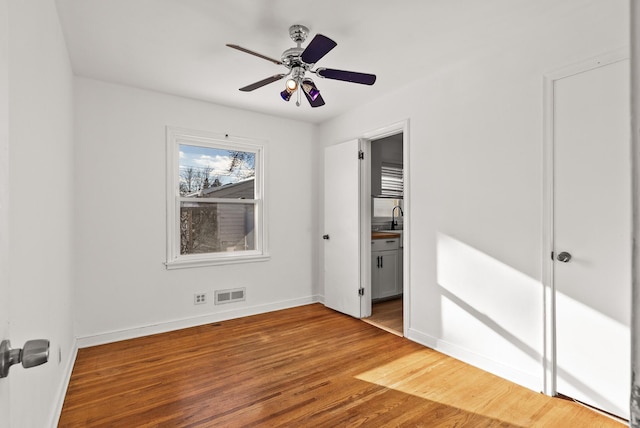 unfurnished bedroom with visible vents, a sink, wood finished floors, connected bathroom, and baseboards