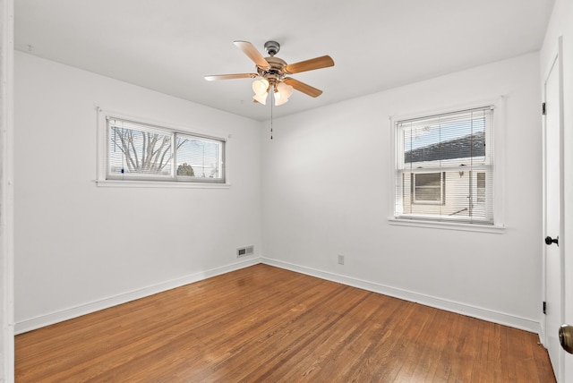 empty room featuring a ceiling fan, wood finished floors, visible vents, and baseboards