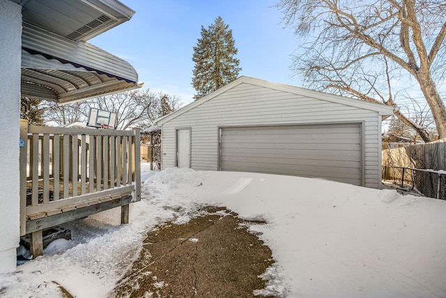 snow covered garage with a garage and fence