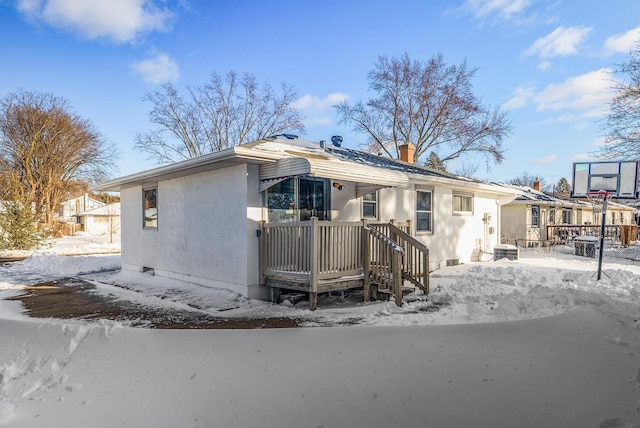 snow covered rear of property featuring stucco siding and a chimney