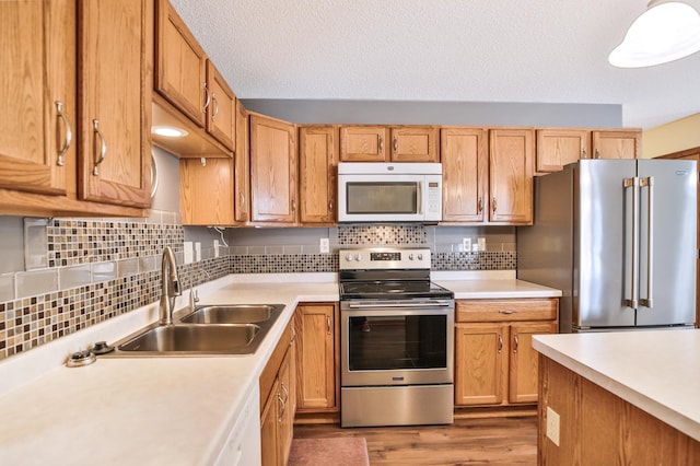 kitchen with appliances with stainless steel finishes, wood finished floors, light countertops, and a sink