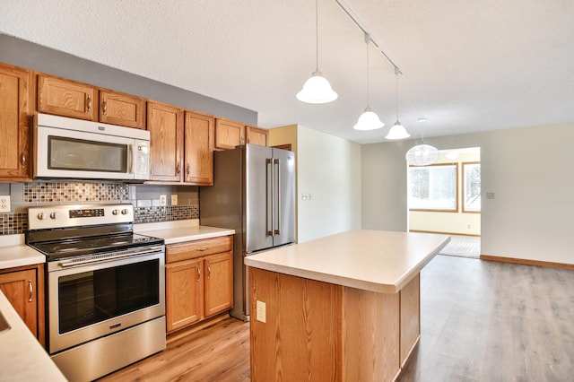 kitchen with light wood finished floors, decorative light fixtures, tasteful backsplash, appliances with stainless steel finishes, and light countertops