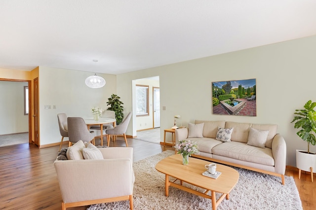 living area featuring light wood-style flooring, a notable chandelier, and baseboards