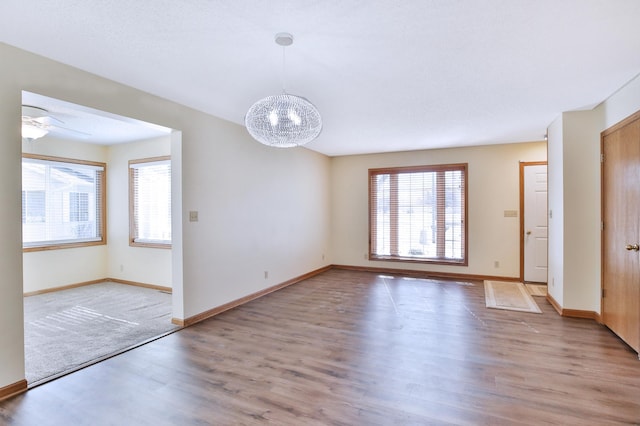 unfurnished room featuring ceiling fan with notable chandelier, baseboards, and wood finished floors