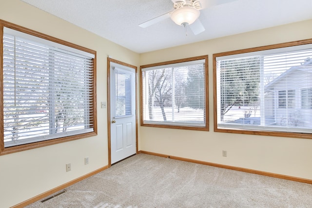 spare room featuring visible vents, light carpet, a textured ceiling, baseboards, and ceiling fan