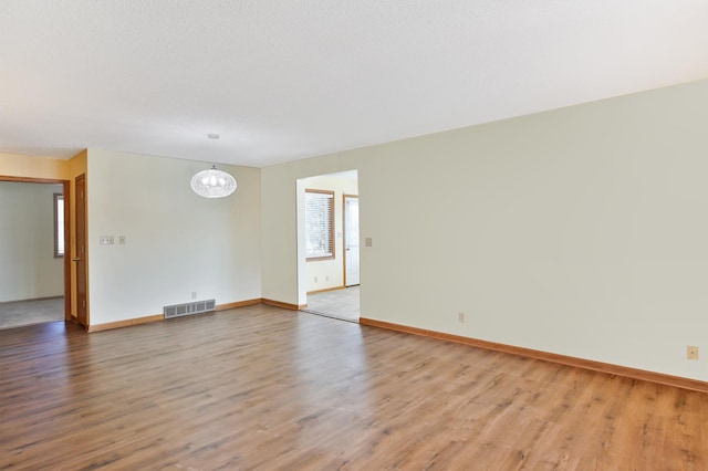 spare room with visible vents, baseboards, a notable chandelier, and light wood-style flooring