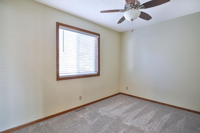 carpeted spare room with a textured ceiling, baseboards, visible vents, and ceiling fan