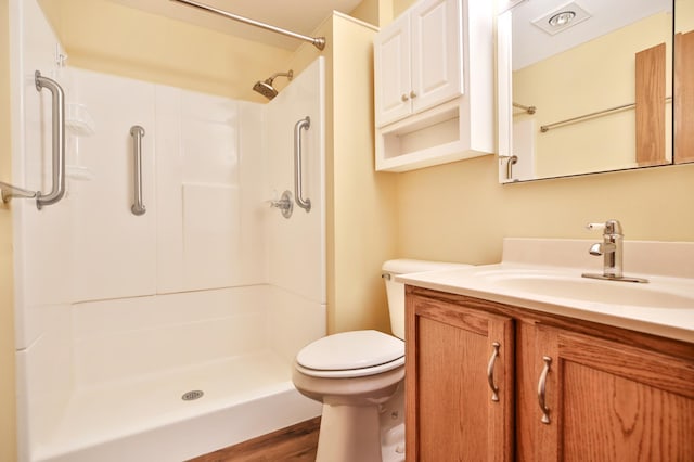 bathroom featuring toilet, walk in shower, wood finished floors, and vanity