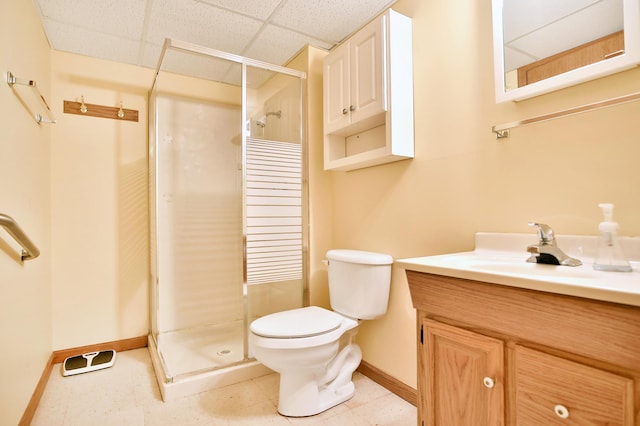 full bath with toilet, a shower stall, a paneled ceiling, baseboards, and vanity