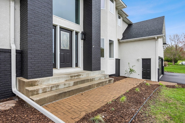 property entrance featuring brick siding, roof with shingles, and stucco siding