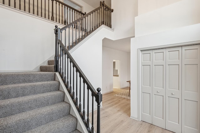 staircase featuring baseboards, a high ceiling, and wood finished floors