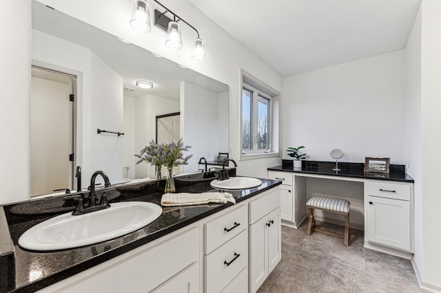 full bath featuring double vanity, a textured ceiling, a sink, and a stall shower