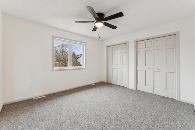 unfurnished bedroom with ceiling fan, visible vents, baseboards, carpet floors, and multiple closets