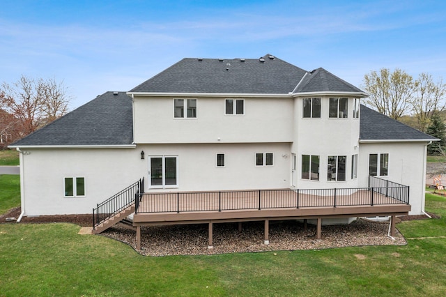 rear view of property with a lawn, a deck, a shingled roof, and stucco siding