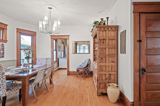 dining room with light wood finished floors, an inviting chandelier, a baseboard heating unit, and baseboards