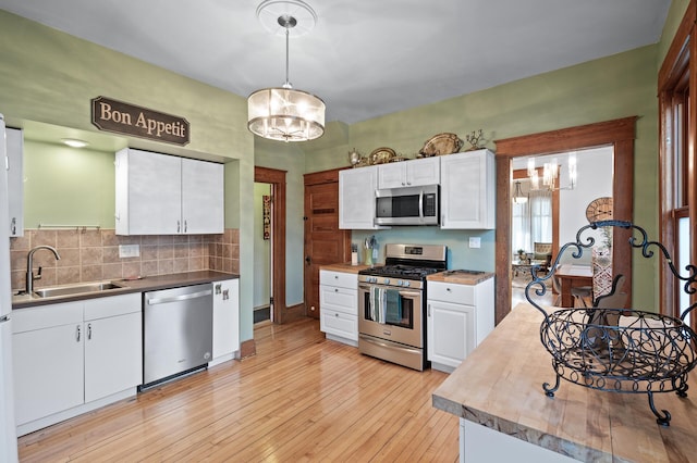 kitchen featuring light wood-type flooring, a sink, white cabinetry, an inviting chandelier, and appliances with stainless steel finishes