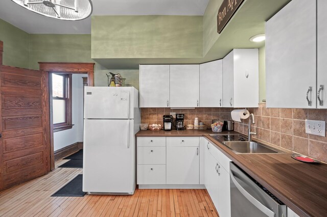 kitchen featuring stainless steel dishwasher, freestanding refrigerator, light wood-style floors, white cabinets, and a sink