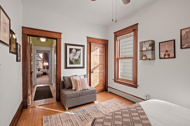 bedroom with a baseboard radiator, baseboards, a ceiling fan, and light wood finished floors