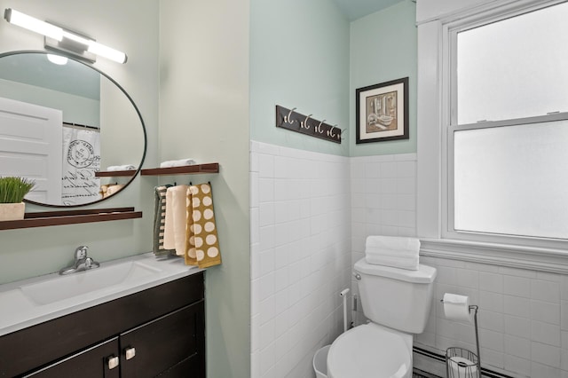 bathroom featuring toilet, vanity, baseboard heating, wainscoting, and tile walls