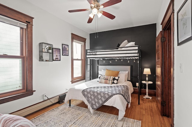 bedroom with ceiling fan, a baseboard radiator, baseboards, and wood finished floors