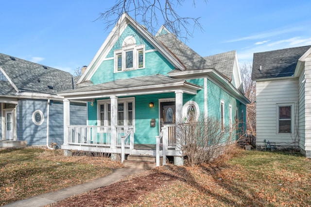 victorian home with a front lawn, covered porch, and roof with shingles