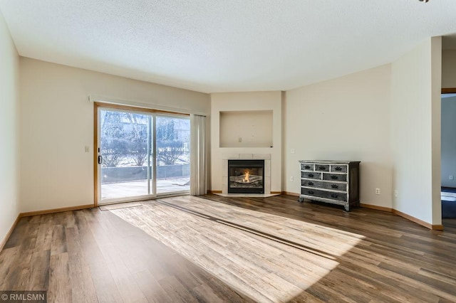 unfurnished living room featuring a textured ceiling, wood finished floors, baseboards, and a tile fireplace