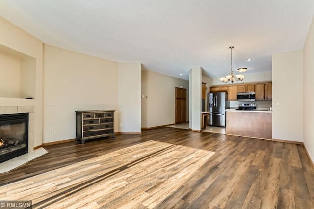 unfurnished living room featuring baseboards, an inviting chandelier, wood finished floors, and a tiled fireplace