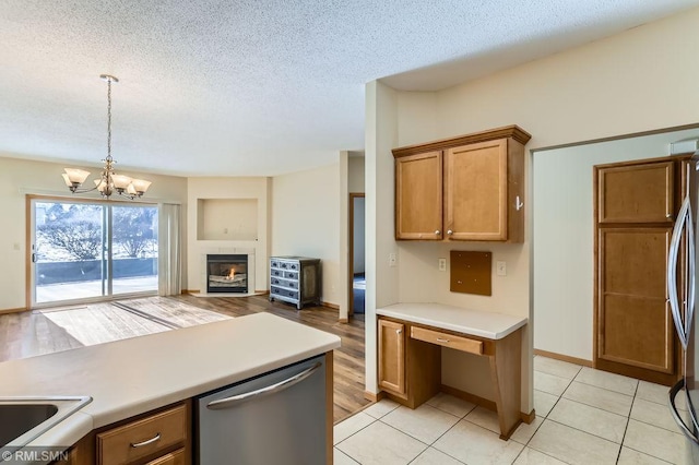 kitchen with brown cabinetry, stainless steel appliances, a textured ceiling, a glass covered fireplace, and decorative light fixtures