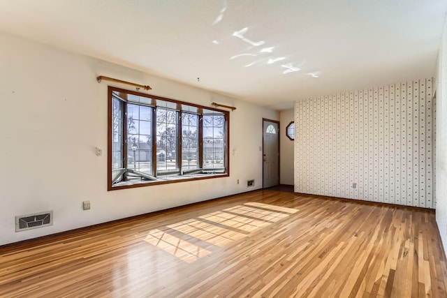 unfurnished room featuring wallpapered walls, wood finished floors, visible vents, and baseboards