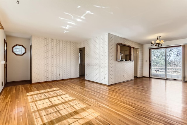 unfurnished living room featuring baseboards, light wood finished floors, a notable chandelier, and wallpapered walls