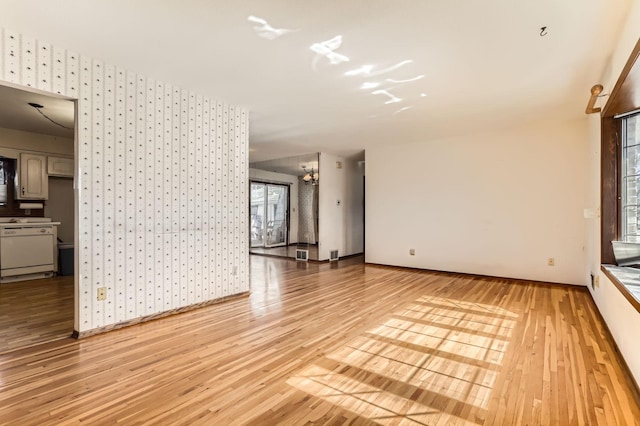 empty room featuring wallpapered walls, light wood-type flooring, and baseboards