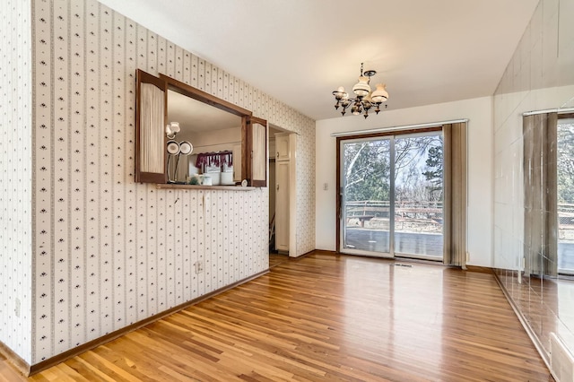 spare room featuring light wood finished floors, a notable chandelier, wallpapered walls, and baseboards