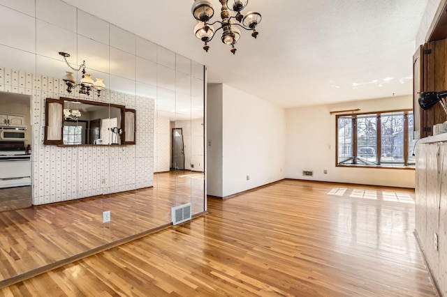 unfurnished living room with visible vents, wood finished floors, baseboards, and a chandelier