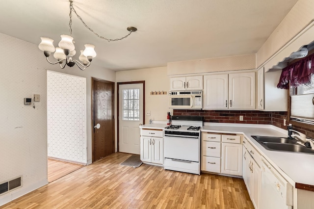 kitchen featuring white appliances, visible vents, wallpapered walls, a sink, and light wood-style floors