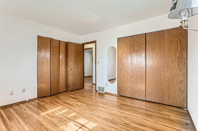 unfurnished bedroom with visible vents, two closets, baseboards, light wood-style flooring, and arched walkways