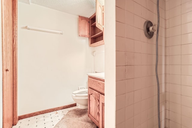 full bathroom featuring toilet, a textured ceiling, a tile shower, baseboards, and vanity