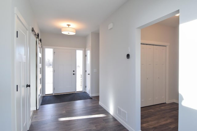 entryway with a barn door, dark wood-style floors, visible vents, and baseboards