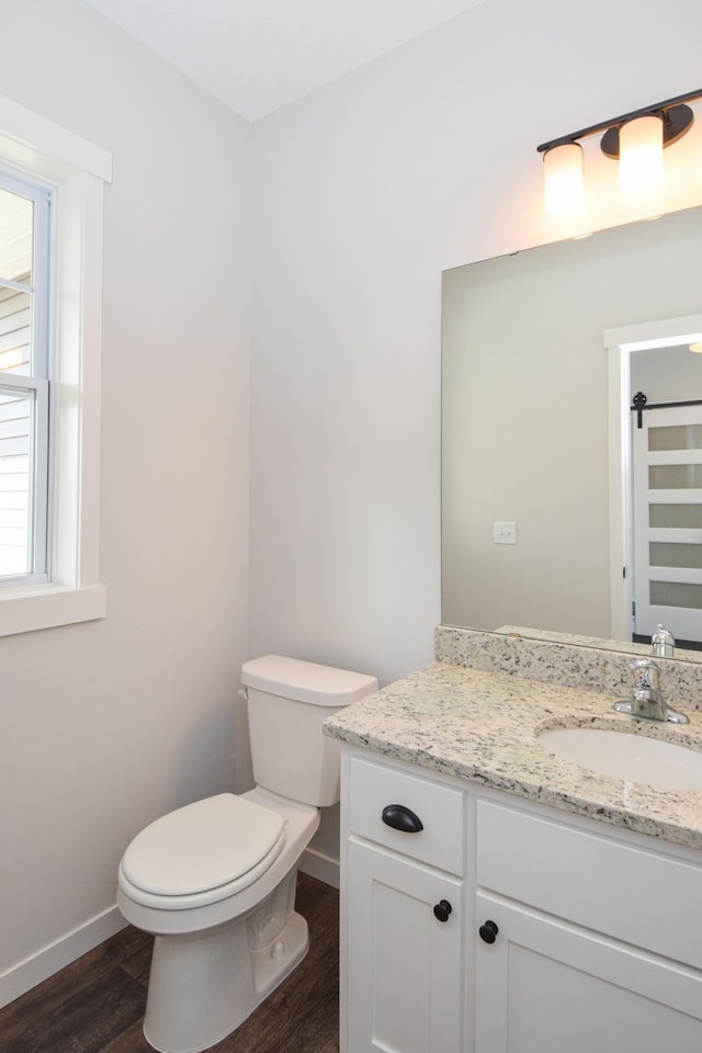 half bathroom with toilet, vanity, baseboards, and wood finished floors