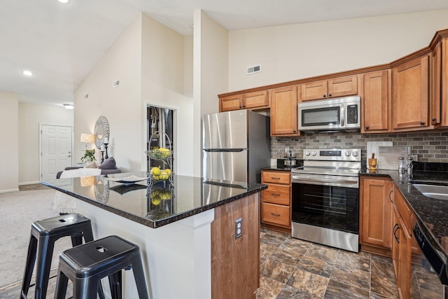 kitchen featuring visible vents, brown cabinets, a breakfast bar, appliances with stainless steel finishes, and decorative backsplash