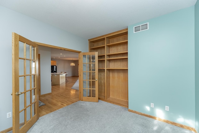 carpeted empty room with french doors, visible vents, wood finished floors, and an inviting chandelier