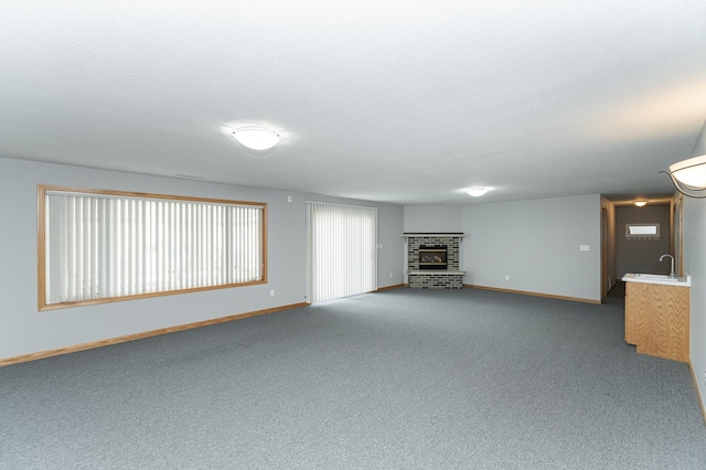 unfurnished living room featuring a textured ceiling, carpet flooring, baseboards, and a sink