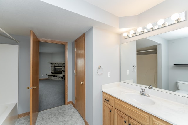 bathroom featuring vanity, baseboards, walk in shower, a brick fireplace, and toilet