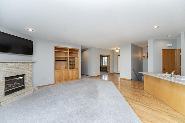 unfurnished living room with visible vents, baseboards, a fireplace, a sink, and light wood-type flooring