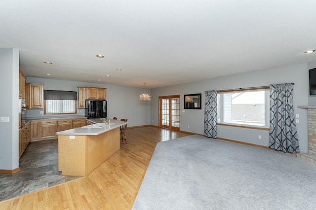 kitchen featuring black fridge with ice dispenser, a center island with sink, plenty of natural light, and light wood-style flooring